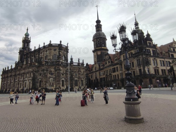 People gather in front of the historic ensemble of buildings in Dresden under a cloudy sky, Dresden