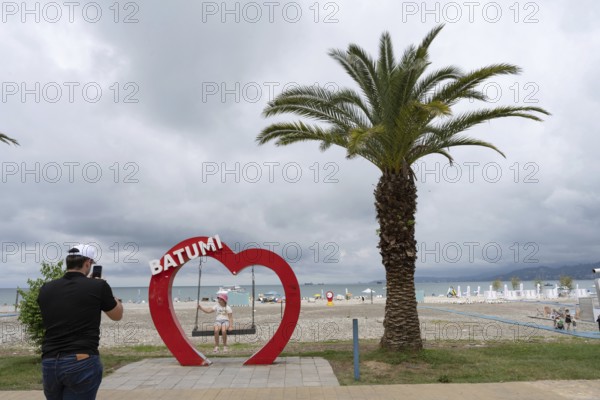 Batumi, Georgia. July 21st 2025. A father takes a photo of his daughter with the heart shaped Batumi sign on the seaside esplanade at the Georgian resort city of Batumi on the Black Sea coast, Georgia