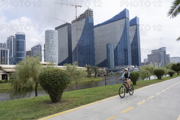 Batumi, Georgia. July 21st 2025. A woman cycles along a dedicated cycle path beside the Georgian Black Sea with modern high-rise holiday apartments under construction in Batumi, Georgia