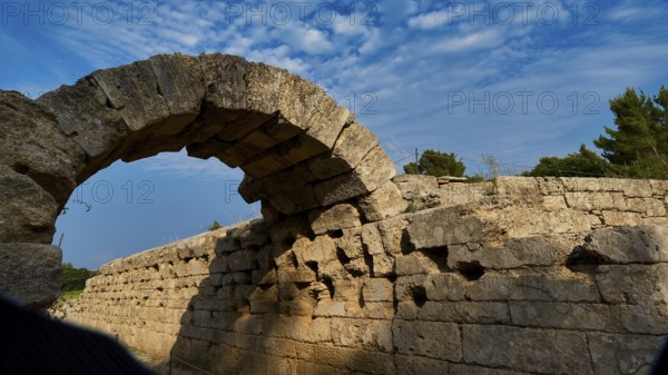 Crypt, vaulted portico, entrance to the stadium, ancient stone arch with shadow cast, surrounded by blue sky, archaeological site, Ancient Olympia, Olympia, Peloponnese, Greece