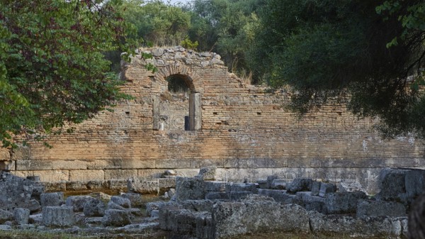 Palestra, red brick wall with an arch surrounded by vegetation and ruined architecture, Archaeological Site, Ancient Olympia, Olympia, Peloponnese, Greece