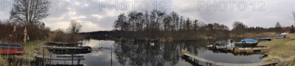 A calm lake with jetties and boats, surrounded by barren vegetation and clear skies, Berlin