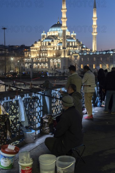 Istanbul, Turkey. January 3rd 2025. Turkish men fishing at night from the Galata Bridge at the mouth of the Bosporus Straight with the illuminated architecture of Yeni Camii the New Mosque, Istanbul, Turkey