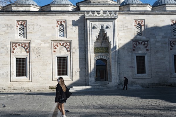 Istanbul, Turkey. January 3rd 2025. A young blond woman walks past a historical mosque near the Istanbul University, Istanbul, Turkey