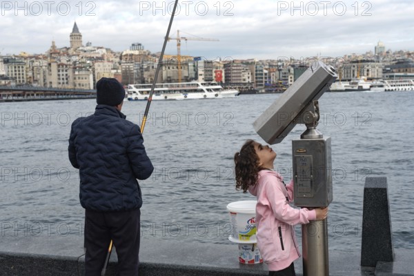 Istanbul, Turkey. January 3rd 2025. A man fishing and a child plays with street binoculars beside the Galata Bridge on the European side of Istanbul, Turkey