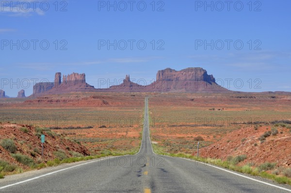 The long, straight road runs through a desert-like landscape with rocks. Access to Monument Valley, Navajo Tribal Park, Navajo Nation Reservation, Utah, Arizona, USA