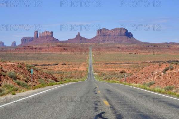 Straight road leads endlessly through a vast desert landscape with rocks in the background, Monument Valley, Navajo Tribal Park, Navajo Nation Reservation, Utah, Arizona, USA