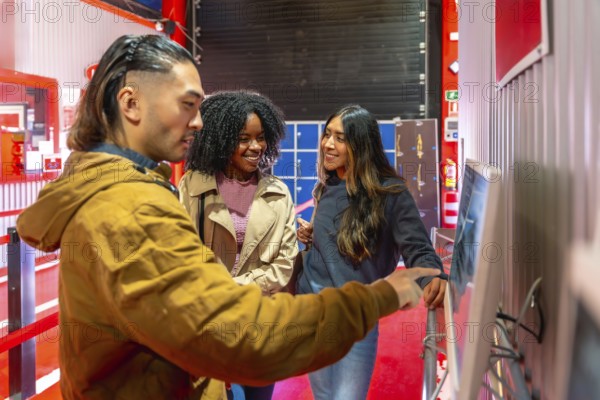 Diverse group of friends smiling and pointing at a touchscreen to select races and book indoor go karting fun, preparing for an energetic, social weekend activity together
