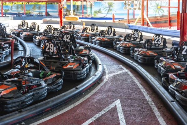 Rows of empty go karts lined up on an indoor race track, engines idle, safety barriers hugging the challenging turns, ready for competitive racing and recreational fun