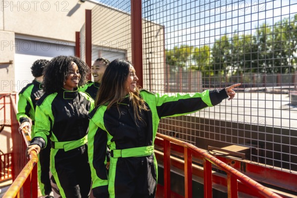 Diverse group of friends in racing suits smiling and pointing at the go kart track, ready for a fun, high energy day of karting, competition and weekend adventure