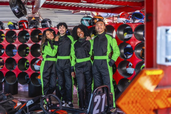 Diverse group of young adult friends smiling and posing in go kart racing suits, ready for an energetic and fun competition at an indoor track and helmet station