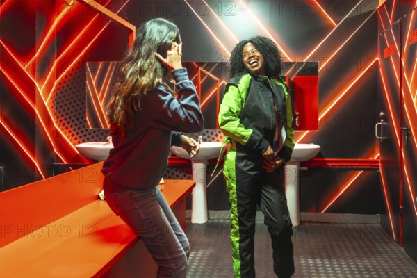 Two friendsone in a racing jumpsuit, the other casuallaugh and bond under vivid red neon in a locker room as they prepare excitedly for a karting session