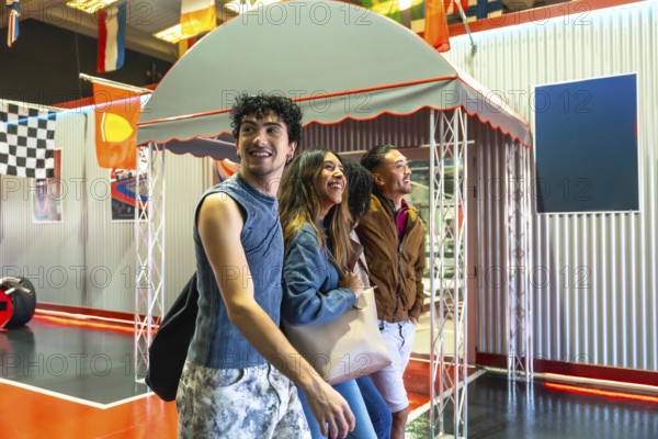 Diverse group of young adult friends smiling and laughing while watching an indoor karting track, preparing for a race or enjoying the excitement of the game