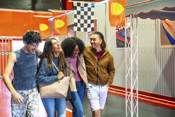 Diverse group of smiling young adult friends having fun and embracing casually while walking together at an indoor karting track, enjoying time spent on entertainment and leisure