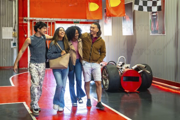 Group of four diverse young adult friends walking together and laughing, finding happiness and enjoying fun leisure time inside an indoor entertainment go karting track