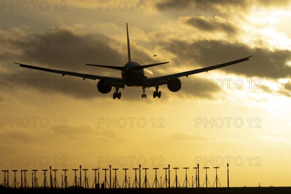 Boeing 777 commercial passenger jet aircraft in flight on approach to land over runway lights silhouette at sunset at London Stansted airport, Essex, England, United Kingdom