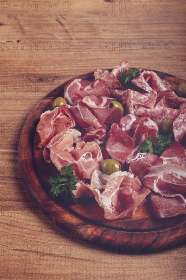 Assortment, sliced meat appetizer, prosciutto, salami and ham, with olives, on a wooden board, breakfast, top view, close-up, no people