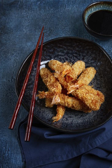 Shrimp in tempura, deep fried, on a black plate, with soy sauce, close-up, top view, no people