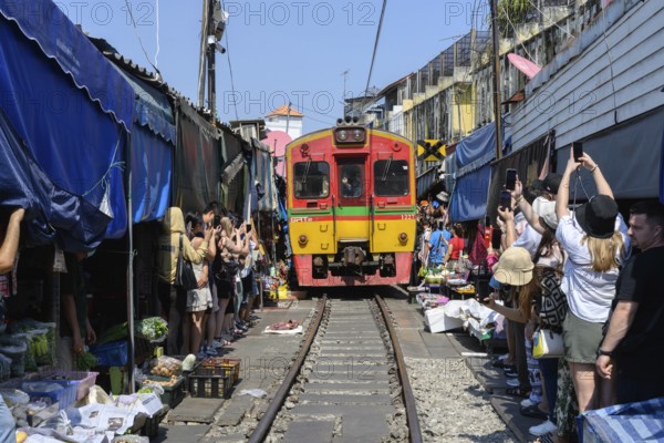 Mae Klong, Thailand. March 15th 2025. Tourists crowd around the arriving 14.30 train as it passes through the Mae Klong Railway market, in Samut Songkhram province of Thailand