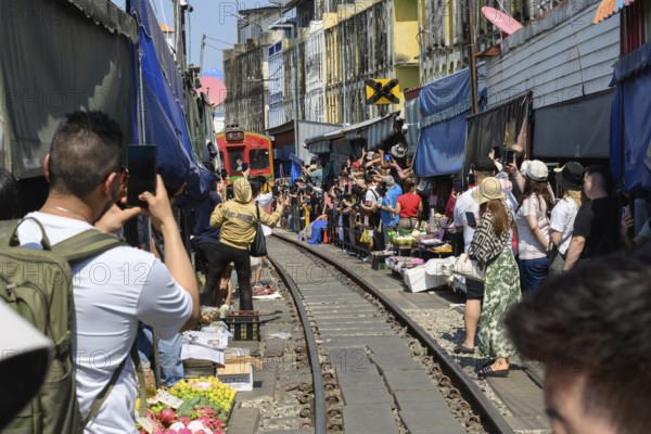 Mae Klong, Thailand. March 15th 2025. Tourists gather on the rail lines as the 14.30 train passes through the Mae Klong Railway market, in Samut Songkhram province of Thailand