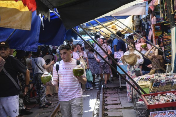 Mae Klong, Thailand. March 15th 2025. Tourists shop for fresh coconut juice at the Mae Klong Railway market, in Samut Songkhram province of Thailand