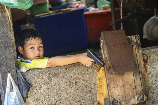 Mae Klong, Thailand. March 15th 2025. A young Thai boy with a toy gun at the Maeklong Railway market, in Samut Songkhram province of Thailand, Asia