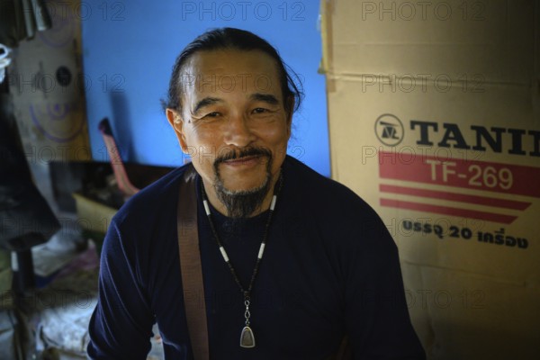 Mae Klong, Thailand. March 15th 2025. A smiling Thai market trader with an amulet necklace, at the Maeklong Railway market, in Samut Songkhram province of Thailand