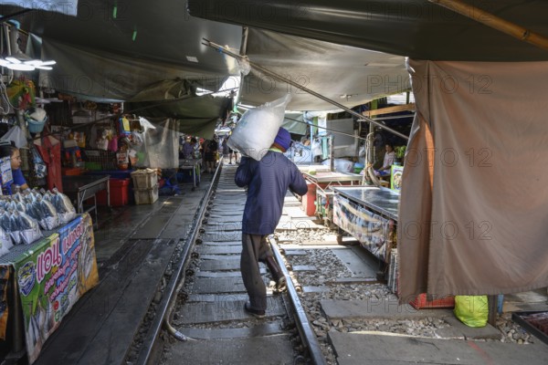 Mae Klong, Thailand. March 15th 2025. A market trader carries a bag of ice in the Maeklong Railway market, in Samut Songkhram province of Thailand