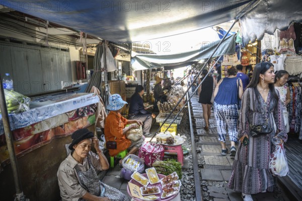 Mae Klong, Thailand. March 15th 2025. Tourists wander along the train rail lines with Thai market traders selling fresh food at the The Mae Klong Train Market in Thailand