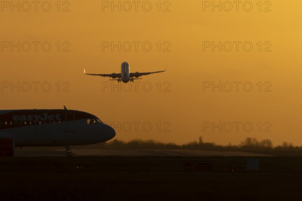 Airbus commercial passenger airliner jet aircraft taking off in flight with another plane on the taxiway at sunset at London Stansted airport, Essex, England, United Kingdom