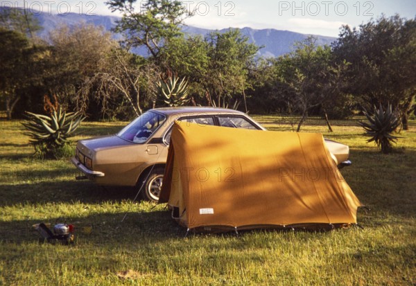 Car and small tent at campsite amongst tropical trees with camp cooking equipment, South Africa, Africa 1979