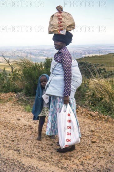 Woman with child and bay on her back, carrying a load on her head, standing in rural area, South Africa, Africa 1979