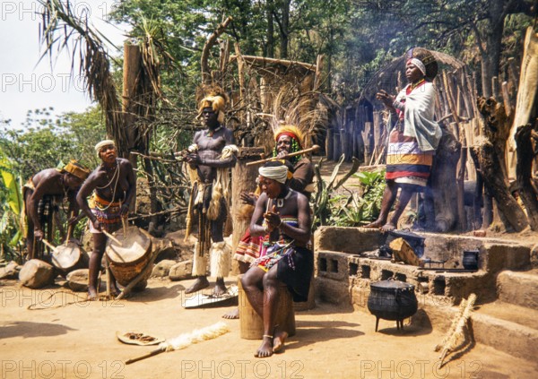 Group of Zulu people dressed in traditional attire, performing an outdoor ceremony at a village, likely in the KwaZulu-Natal province of South Africa