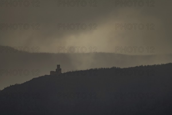 The structure is on a mountain. The sky is cloudy and sunlight is shining in the distance. The scenery shows a dark and mysterious atmosphere. Bas Rhin, Alsace, France