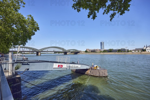 Pier, gangway, Cologne-Düsseldorfer Deutsche Rheinschiffahrt GmbH, Rhine river, MaxCologne high-rise building, Hohenzollern bridge, arched bridge, steel arches, general architecture, wharf, branches, trees, water surface with small waves, blue sky, cloudless, Leystapelwerft, Cologne, district-free city, North Rhine-Westphalia, Germany