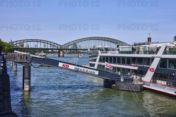 Rhine river, excursion boat, gangway, Cologne-Düsseldorfer Deutsche Rheinschiffahrt GmbH, bridge, Hohenzollern bridge, general architecture, trees, blue sky, cloudless, Leystapelwerft, Cologne, district-free city, North Rhine-Westphalia, Germany