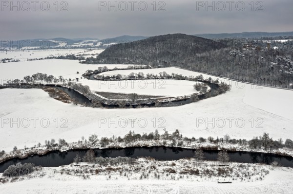 Snow-covered fields with a gently rolling river, surrounded by hills and trees in cloudy skies, The Meanders of the Werra between Hesse and Thuringia in the Werra Valley near Herleshausen