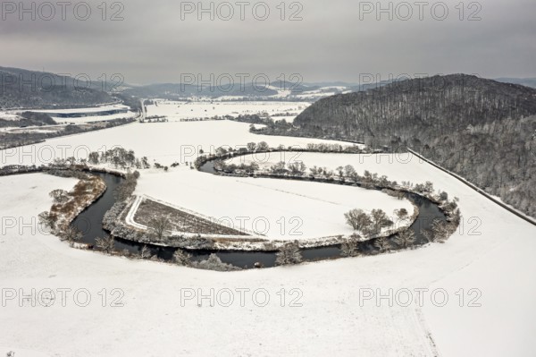 River flows in a loop through snow-covered fields, framed by hills and trees under cloudy skies, The Meanders of the Werra between Hesse and Thuringia in the Werra Valley near Herleshausen