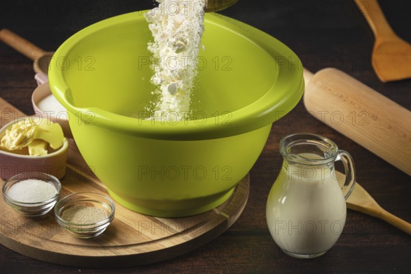 Flour falls into a green bowl surrounded by baking ingredients