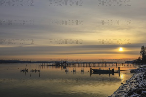 A jetty stretches into a calm lake at sunrise, boats rest on the shore, the sky is yellow and gray, Lake Constance, Lake Zell, Iznang, Höri Peninsula, Konstanz district, Baden-Württemberg, Germany