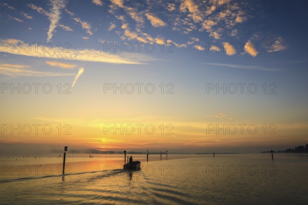 A fishing boat glides through Lake Zell at sunrise, the sky is decorated with clouds, moss, Höri peninsula, Radolfzell, Konstanz district, Baden-Württemberg, Germany