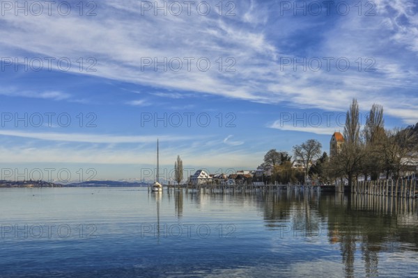 Calm lake in winter with a sailboat on the shore, surrounded by houses and trees, under a cloudy blue sky, Lake Constance, Überlinger See, Bodman-Ludwigshafen, Konstanz district, Baden-Württemberg, Germany