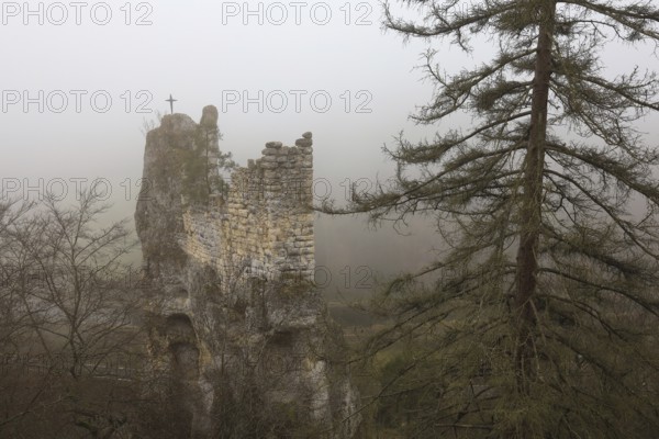 An abandoned castle ruin in fog with a cross on the tower, surrounded by trees and an autumnal atmosphere, Gruene Gutenstein ruins, Obere Donau nature park Park, Inzigkofen, Dietfurt, Sigmaringen district, Baden-Württemberg, Germany