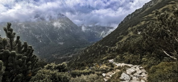Wild mountain trail with a view of a lake, Morskie Oko and thick, dramatic clouds above the peaks, hiking in the High Tatras National Park, Carpathian Mountains, Poland