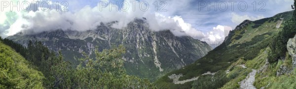 A trail leads through impressive mountain scenery, panoramic peaks covered with green slopes and clouds, hiking in the High Tatras National Park, Carpathian Mountains, Poland