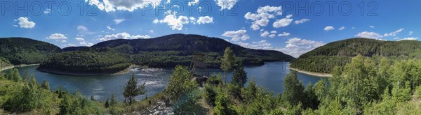 Panoramic view of Leibis Reservoir surrounded by forests and hills under a blue sky, hiking in the Thuringia National Park, Germany