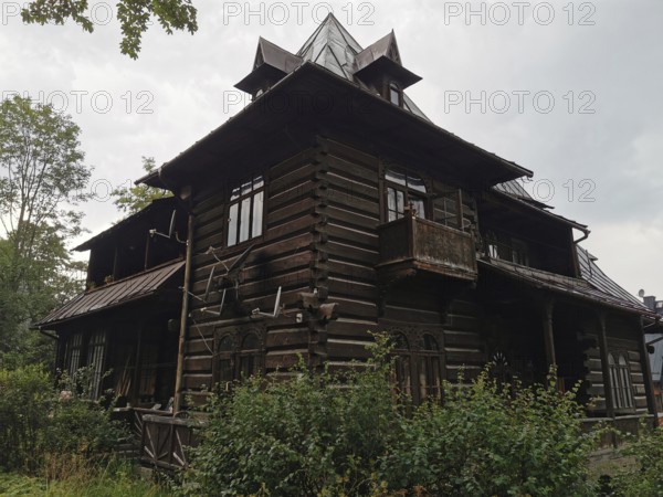 Old typical traditional Tatra wooden house with rustic architecture surrounded by trees under cloudy sky, Zakopane, hiking in the High Tatras National Park, Carpathian Mountains, Poland