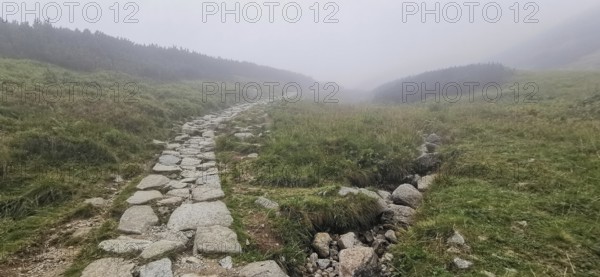 Rocky hiking trail through hilly, foggy landscape, Zakopane, hike to Kasprowy Wierch in the High Tatras National Park, Carpathian Mountains, Poland