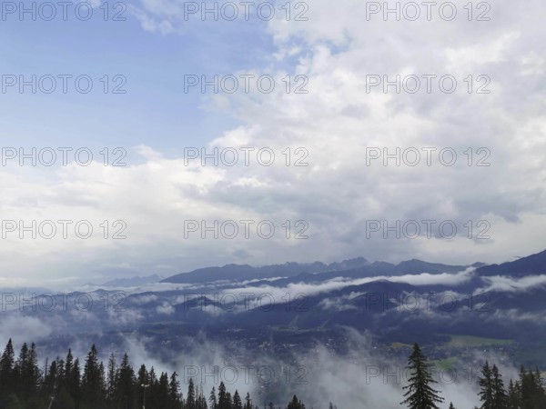 Extensive view of a foggy valley with mountains and cloud cover in the background, Zakopane, hiking in the High Tatras National Park, Carpathian Mountains, Poland