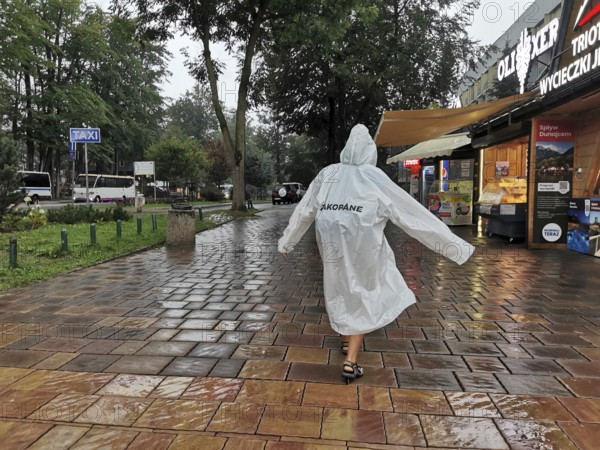 Person in raincoat with Zakopane inscription walking on wet sidewalk in rainy weather, Zakopane, hiking in the High Tatras National Park, Carpathian Mountains, Poland